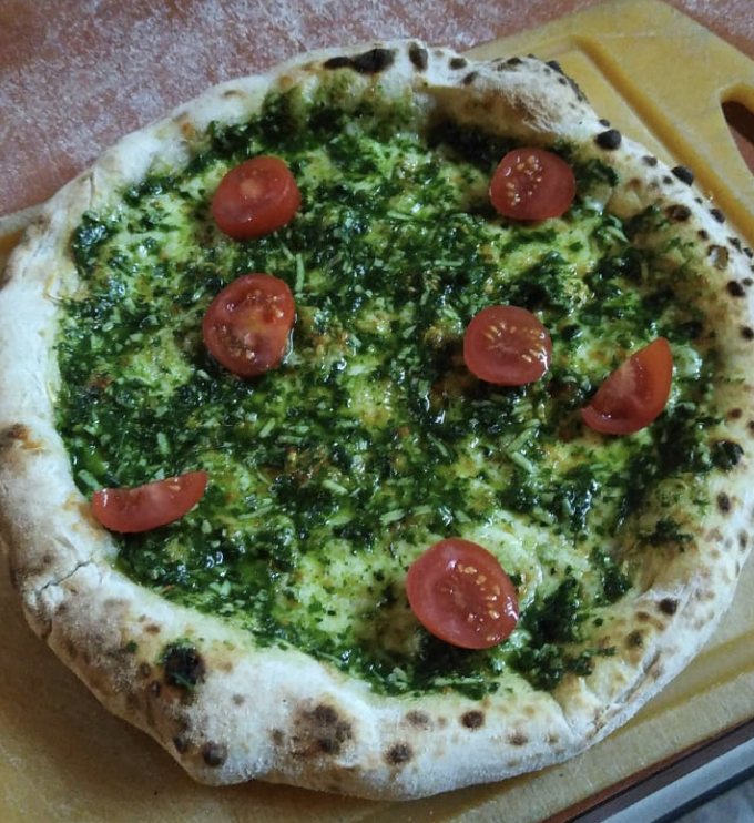 Pizza vegetariana al pesto con tomates cherry sobre tabla de madera
